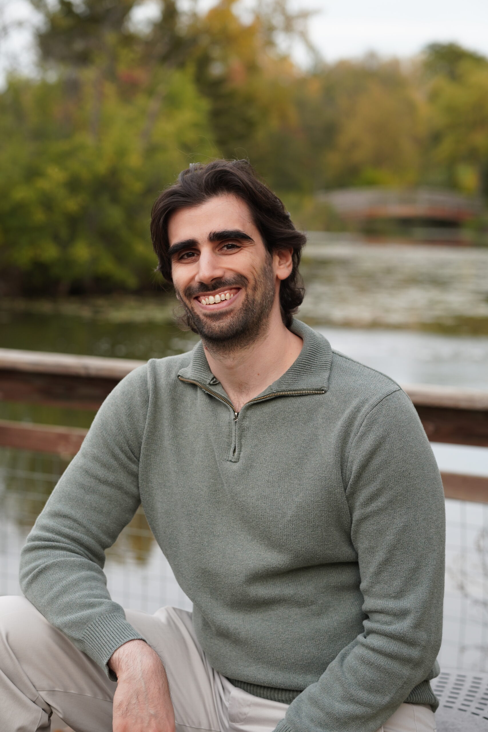 A portrait of myself, Dr. Sami Daniel, sitting outside with a lake and trees in the background.